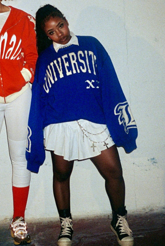 Two people wearing oversized sweatshirts in a room with a white wall.