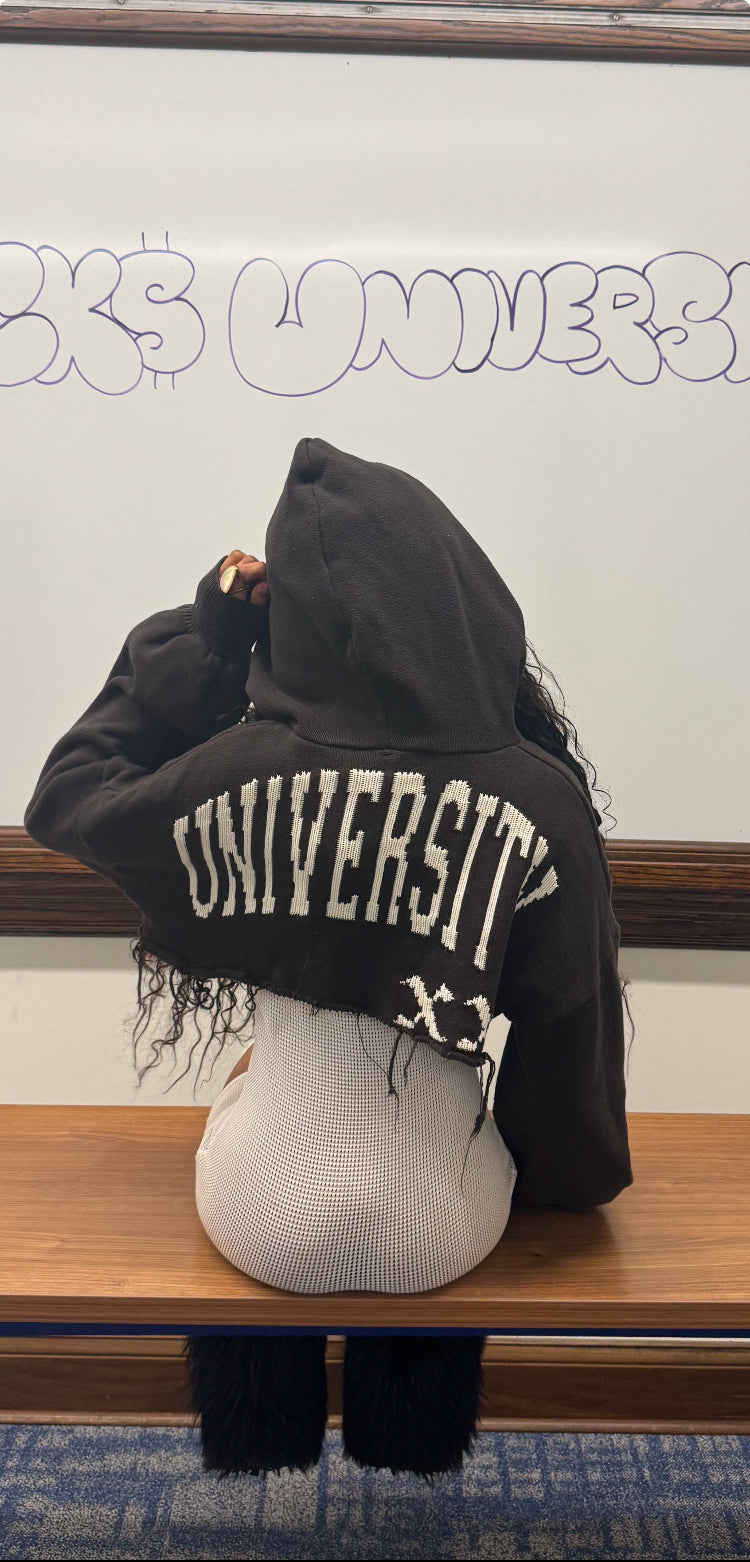 Person wearing a dark hoodie with 'UNIVERSITY' printed on the back, sitting on a bench.