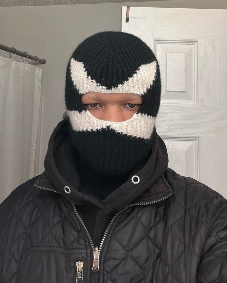 Person wearing a black and white knit balaclava in front of a neutral background