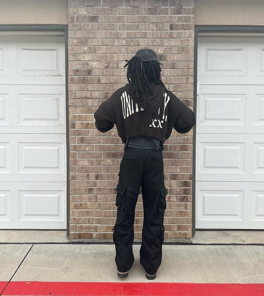 Person wearing a black hoodie with "UNIVERSITY" text standing in front of a brick wall.
